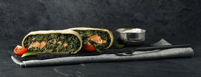 Photo of Pieces of delicious strudel with salmon and spinach served on dark textured table. Space for text