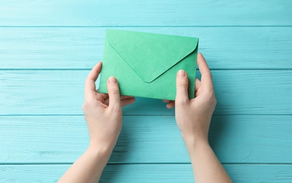 Woman with green paper envelope at light blue wooden table, top view