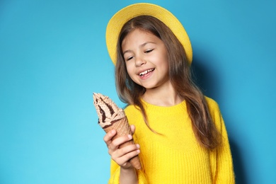 Cute little girl with delicious ice cream against color background, space for text