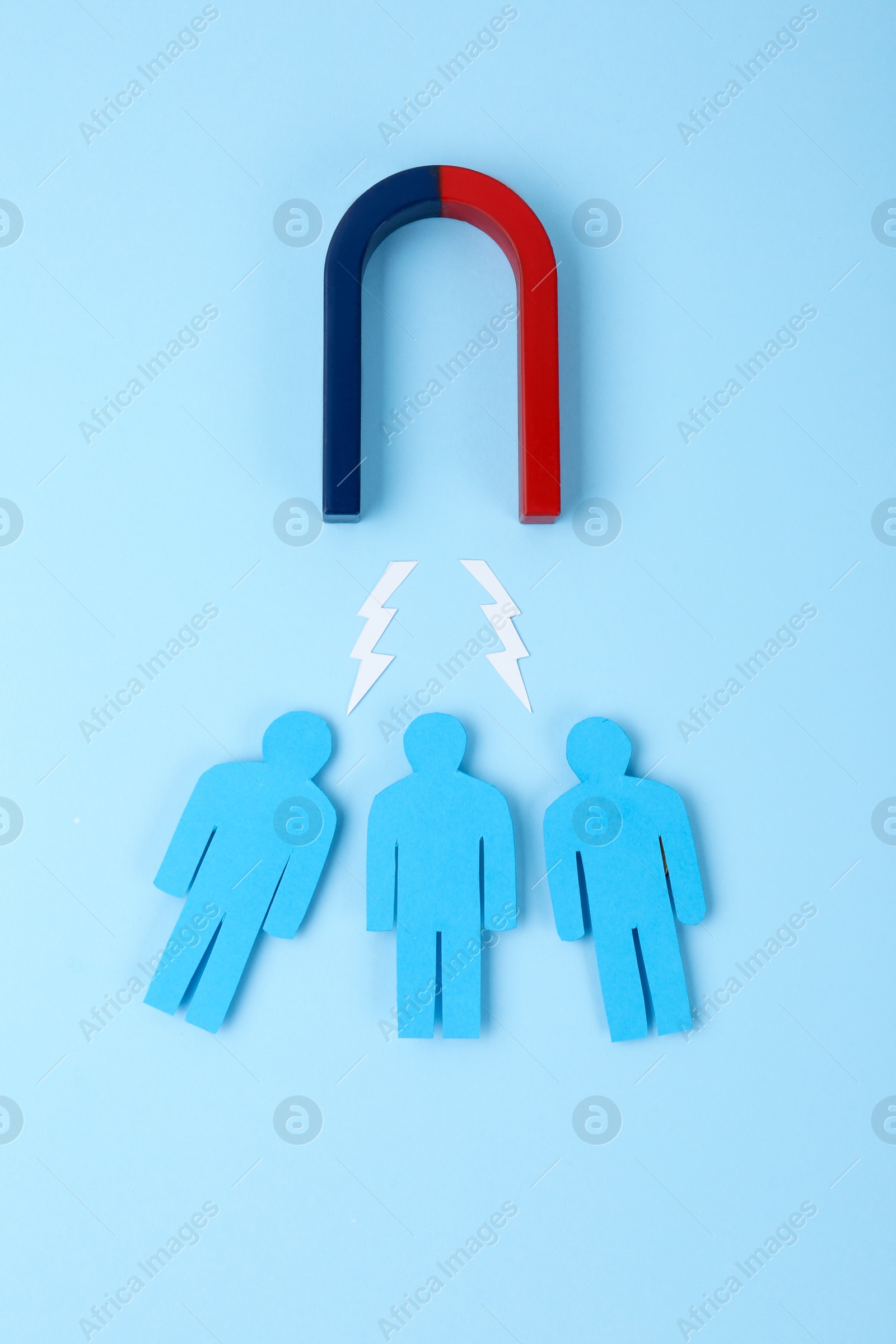 Photo of Magnet attracting paper people on light blue background, flat lay