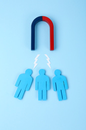 Magnet attracting paper people on light blue background, flat lay