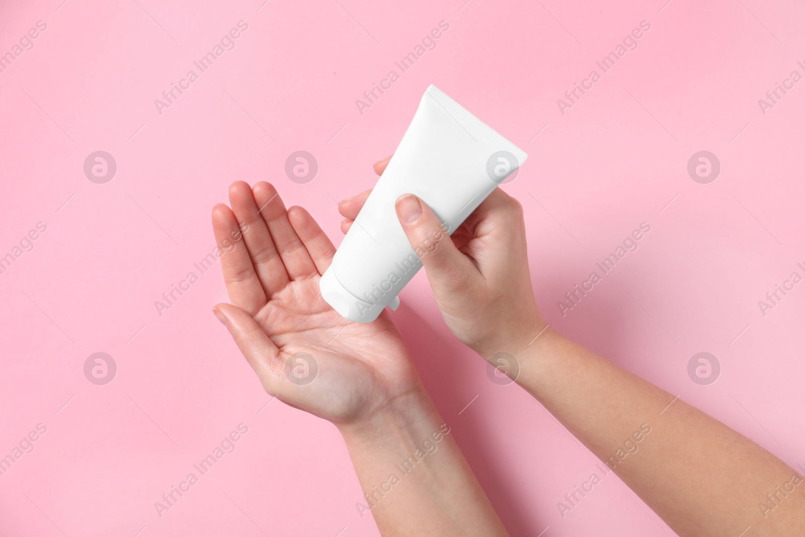 Photo of Woman with tube of hand cream on pink background, top view