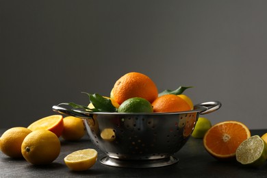 Photo of Fresh citrus fruits in colander on dark table, closeup