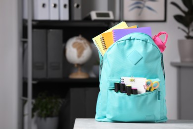 Photo of Turquoise backpack with different school stationery on table indoors, space for text