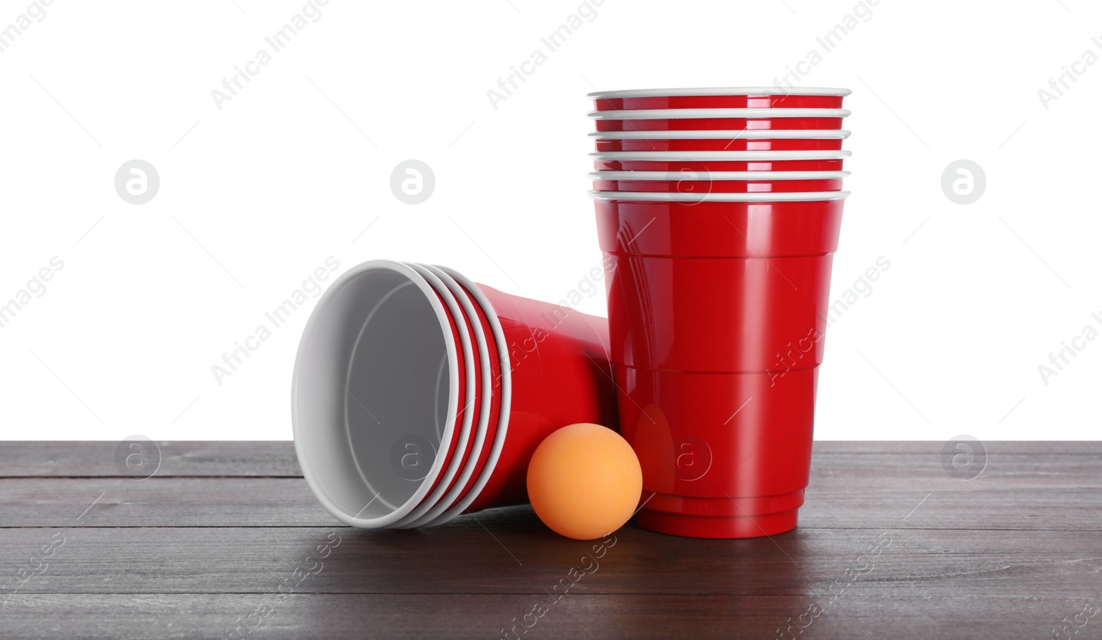 Photo of Plastic cups and ball for beer pong on wooden table against white background