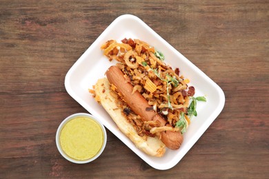 Photo of Fresh delicious hot dog with sauce on wooden table, flat lay