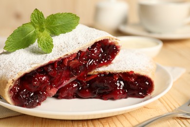 Photo of Delicious strudel with cherries, powdered sugar and mint on wooden table, closeup