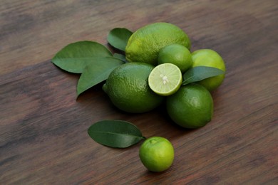 Photo of Whole and cut fresh ripe limes with green leaves on wooden table