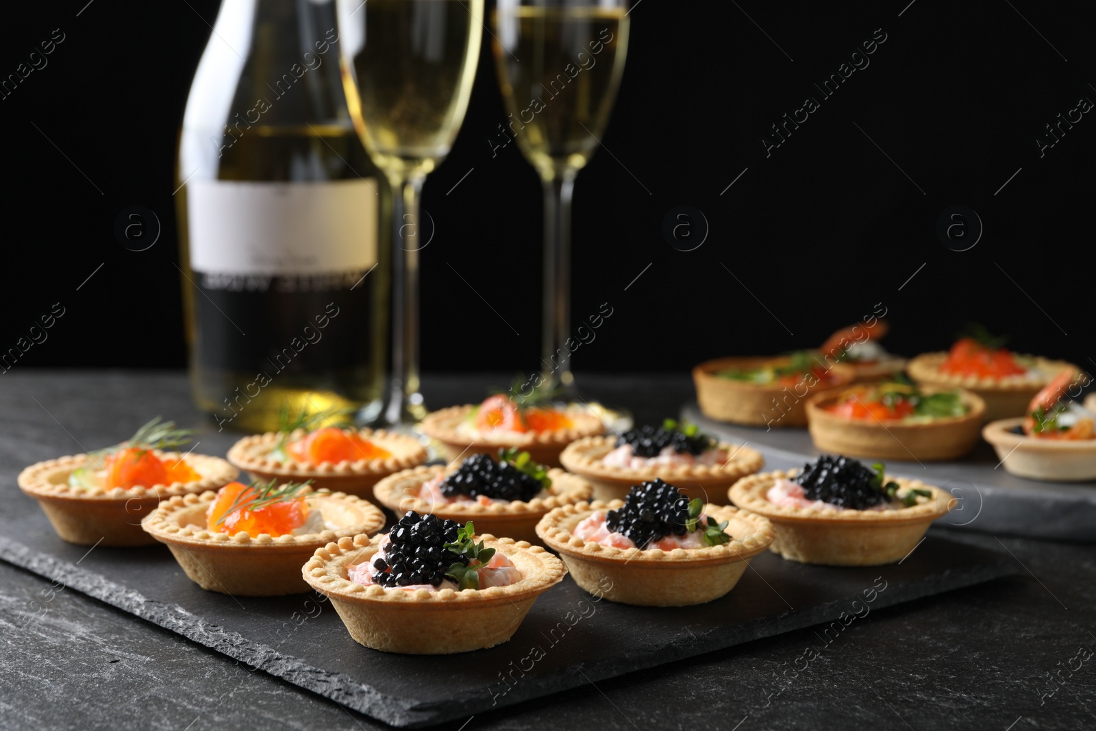 Photo of Delicious canapes with salmon and caviar on black textured table, closeup