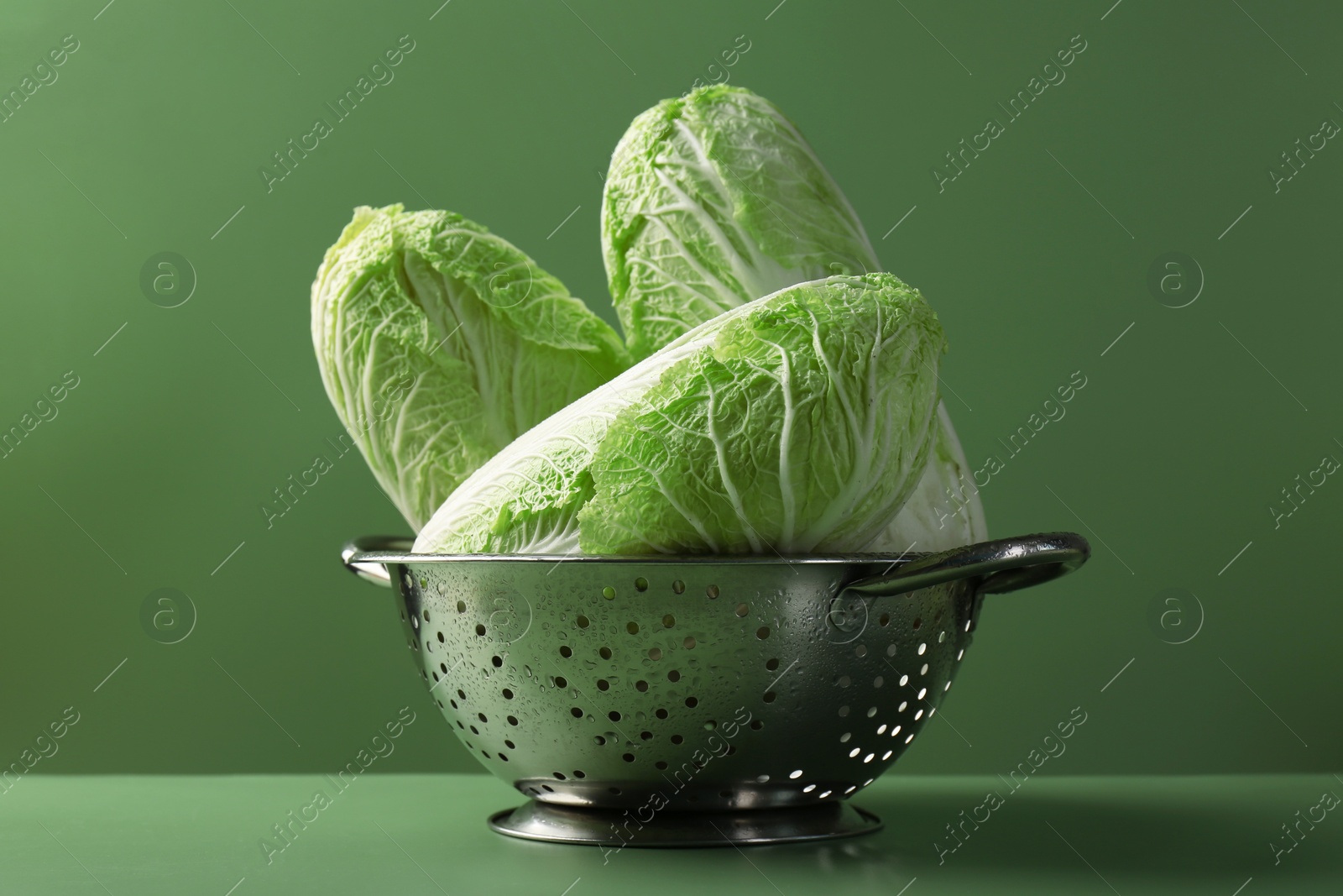 Photo of Fresh Chinese cabbages in colander on green background, closeup