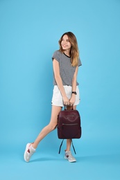 Happy woman with backpack on light blue background