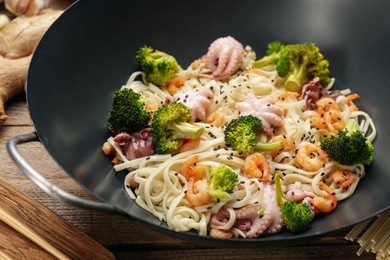 Stir fried noodles with seafood and vegetables in wok on wooden table, closeup