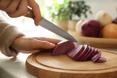 Photo of Woman cutting red onion into slices at countertop in kitchen, closeup