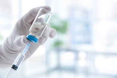 Doctor with syringe and medicine for vaccination on blurred background