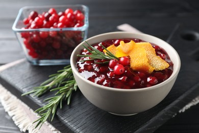 Photo of Fresh cranberry sauce, rosemary and orange peel in bowl on table, closeup