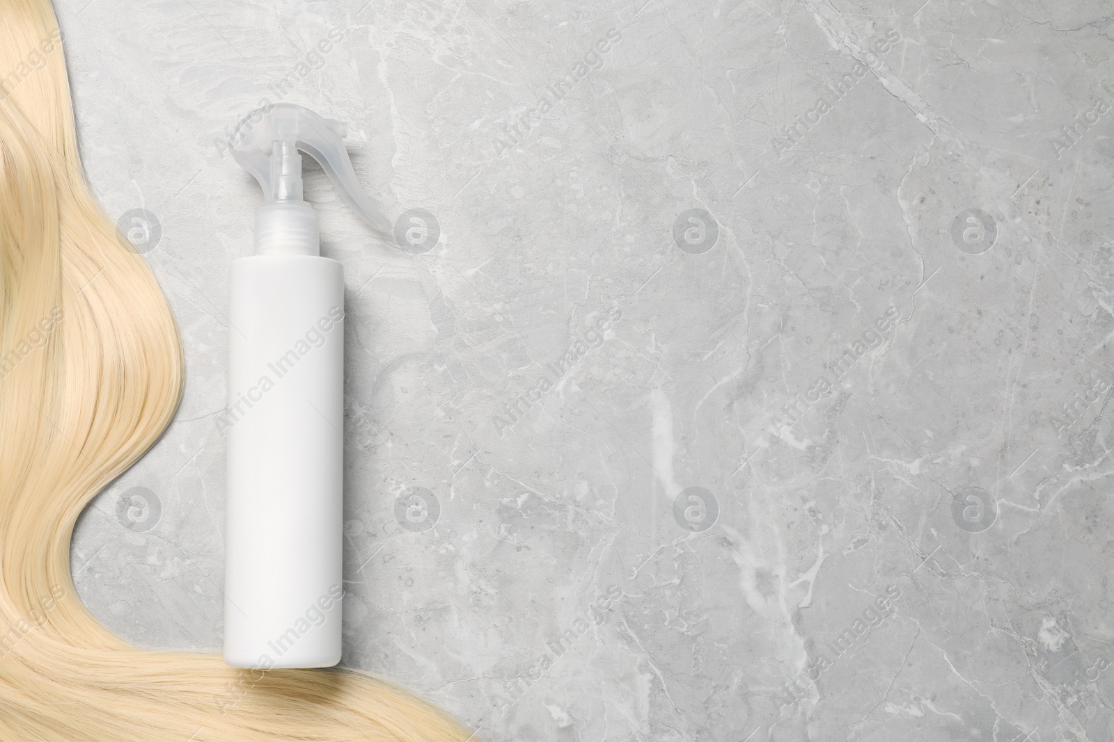 Photo of Spray bottle with thermal protection and lock of blonde hair on grey marble table, flat lay. Space for text