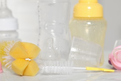 Photo of Clean baby bottles after sterilization near brushes on white table, closeup