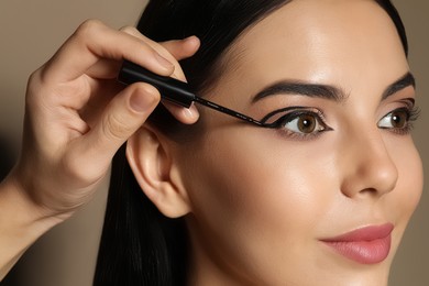 Artist applying black eyeliner onto woman's face on beige background, closeup