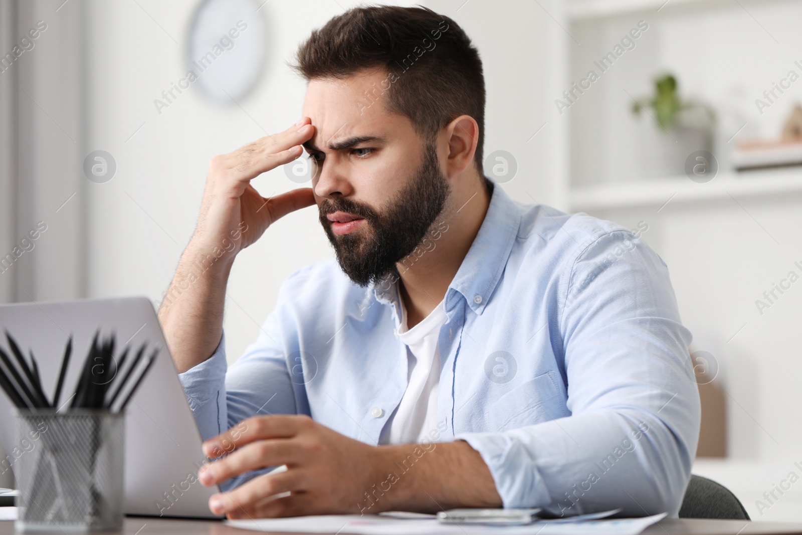 Photo of Man suffering from headache at workplace in office