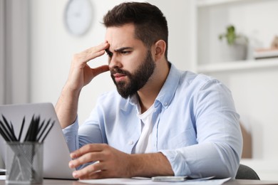 Photo of Man suffering from headache at workplace in office