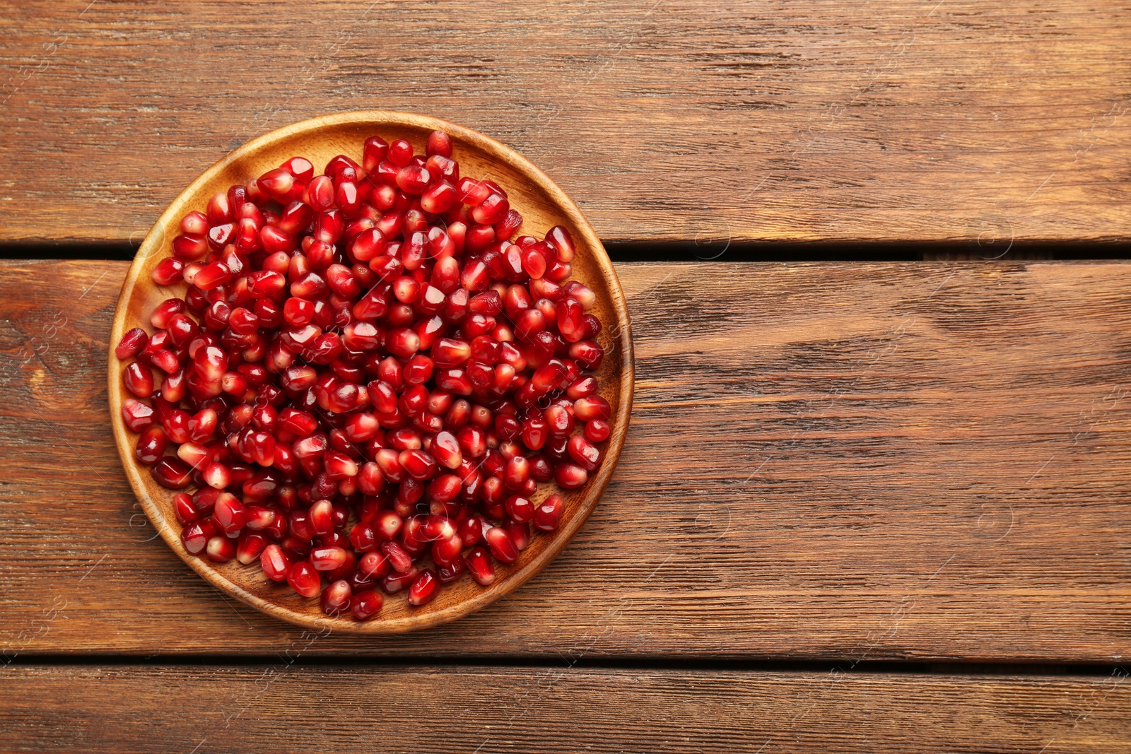 Photo of Tasty ripe pomegranate grains on wooden table, top view. Space for text