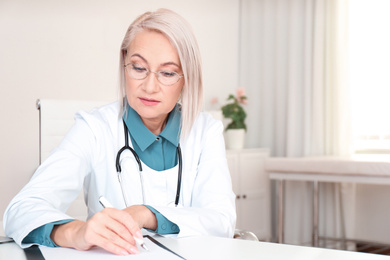Photo of Mature female doctor working at table in office