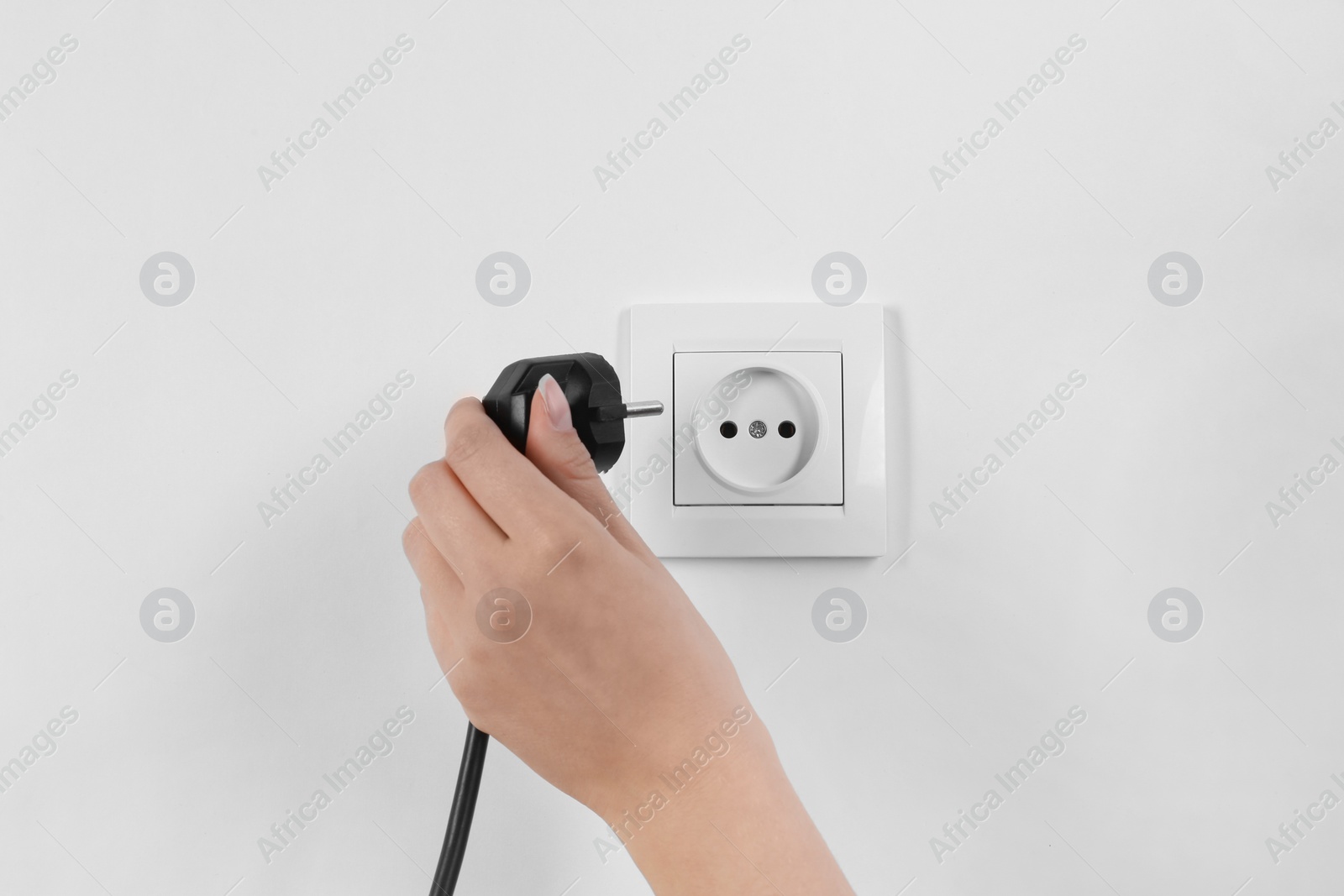 Photo of Woman putting plug into power socket on white background, closeup. Electrician's equipment