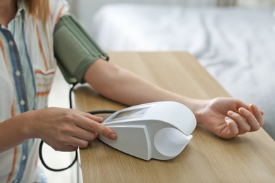 Woman checking blood pressure with sphygmomanometer at table indoors, closeup. Cardiology concept