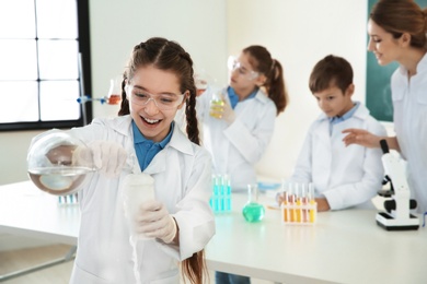 Photo of Schoolgirl making experiment with teacher and pupils in chemistry class