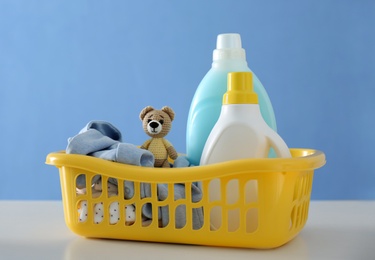 Photo of Detergents and children's clothes on white table near blue wall