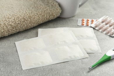 Mustard plasters, pills, thermometer and towel on light grey table, closeup