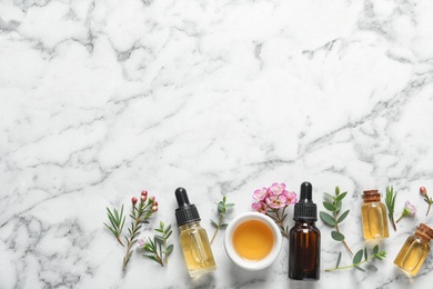 Flat lay composition with bottles of natural tea tree oil and space for text on white marble background