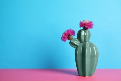 Trendy cactus shaped ceramic vase with flowers on table against color background