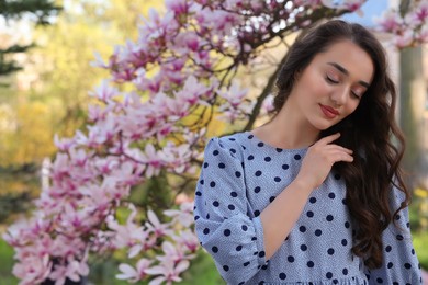 Photo of Beautiful woman near blossoming magnolia tree on spring day, space for text