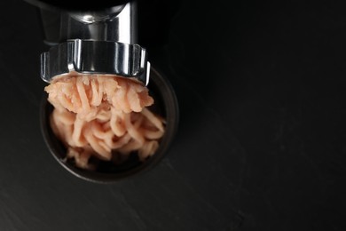 Photo of Electric meat grinder with chicken mince on black table, top view. Space for text