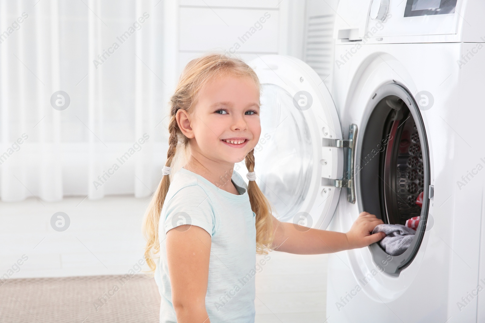 Photo of Adorable little girl doing laundry at home. Space for text