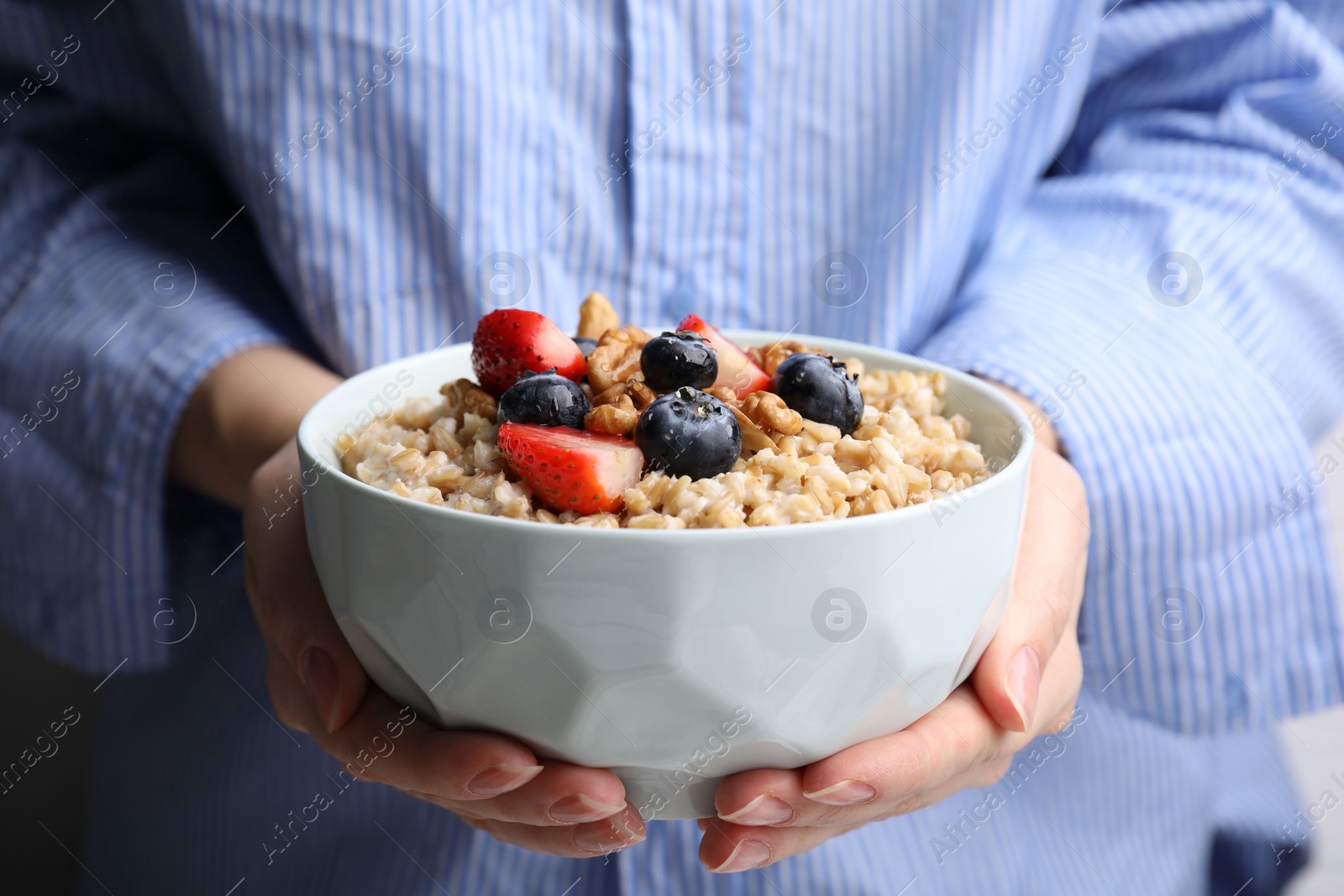 Photo of Woman holding bowl of tasty oatmeal with strawberries, blueberries and walnuts, closeup