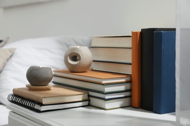 Photo of Hardcover books and scented candles on white bedside table indoors