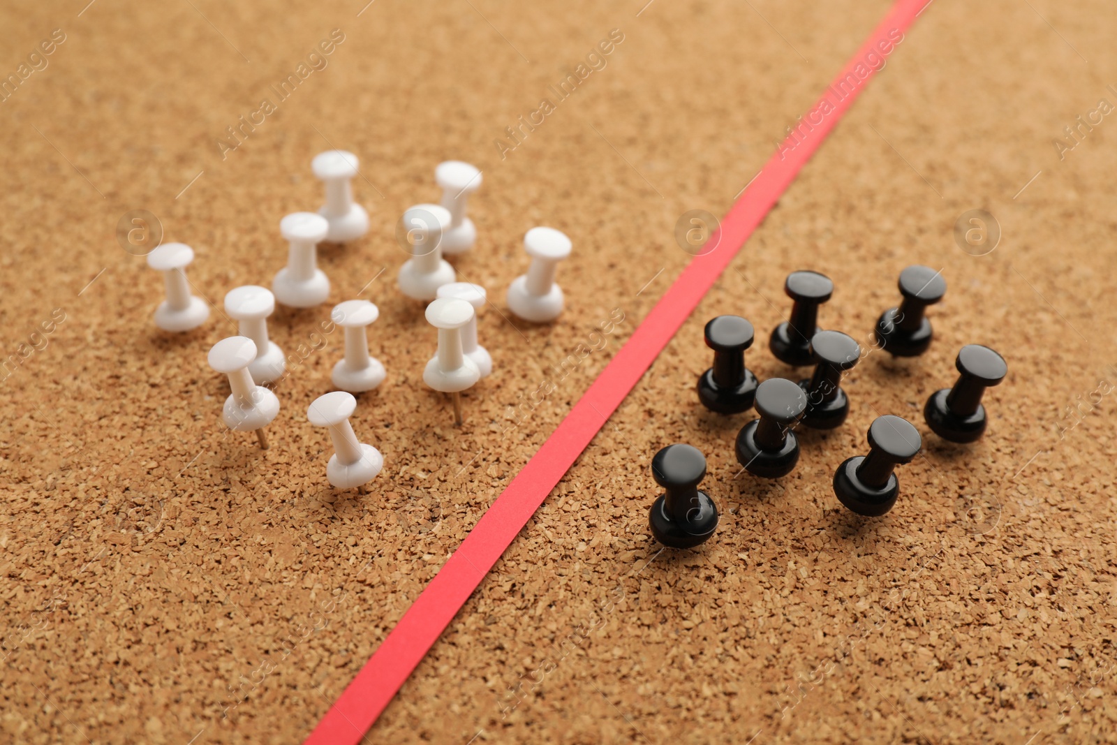Photo of Black and white push pins divided by red strip in cork board. Racism concept