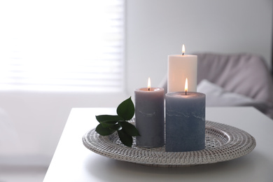 Tray with burning candles and leaves on white table indoors. Space for text