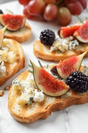 Photo of Bruschettas with cheese, figs and blackberries served on white table, closeup