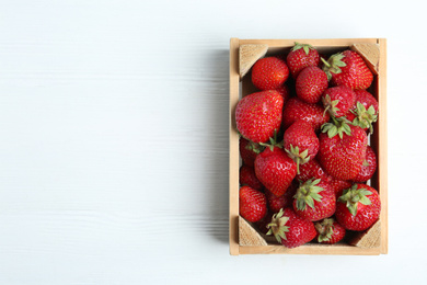 Photo of Delicious ripe strawberries in crate on white wooden table, top view. Space for text