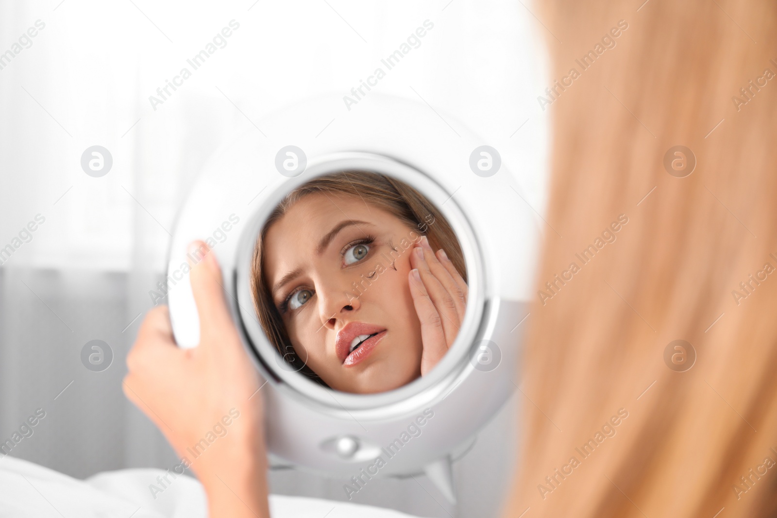 Photo of Young woman with eyelash loss problem looking in mirror indoors