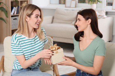 Smiling young woman presenting gift to her friend at home