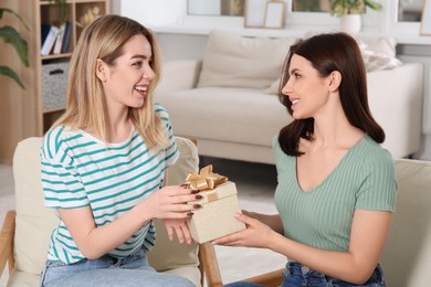 Photo of Smiling young woman presenting gift to her friend at home