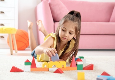 Photo of Cute little child playing with building blocks on floor, indoors