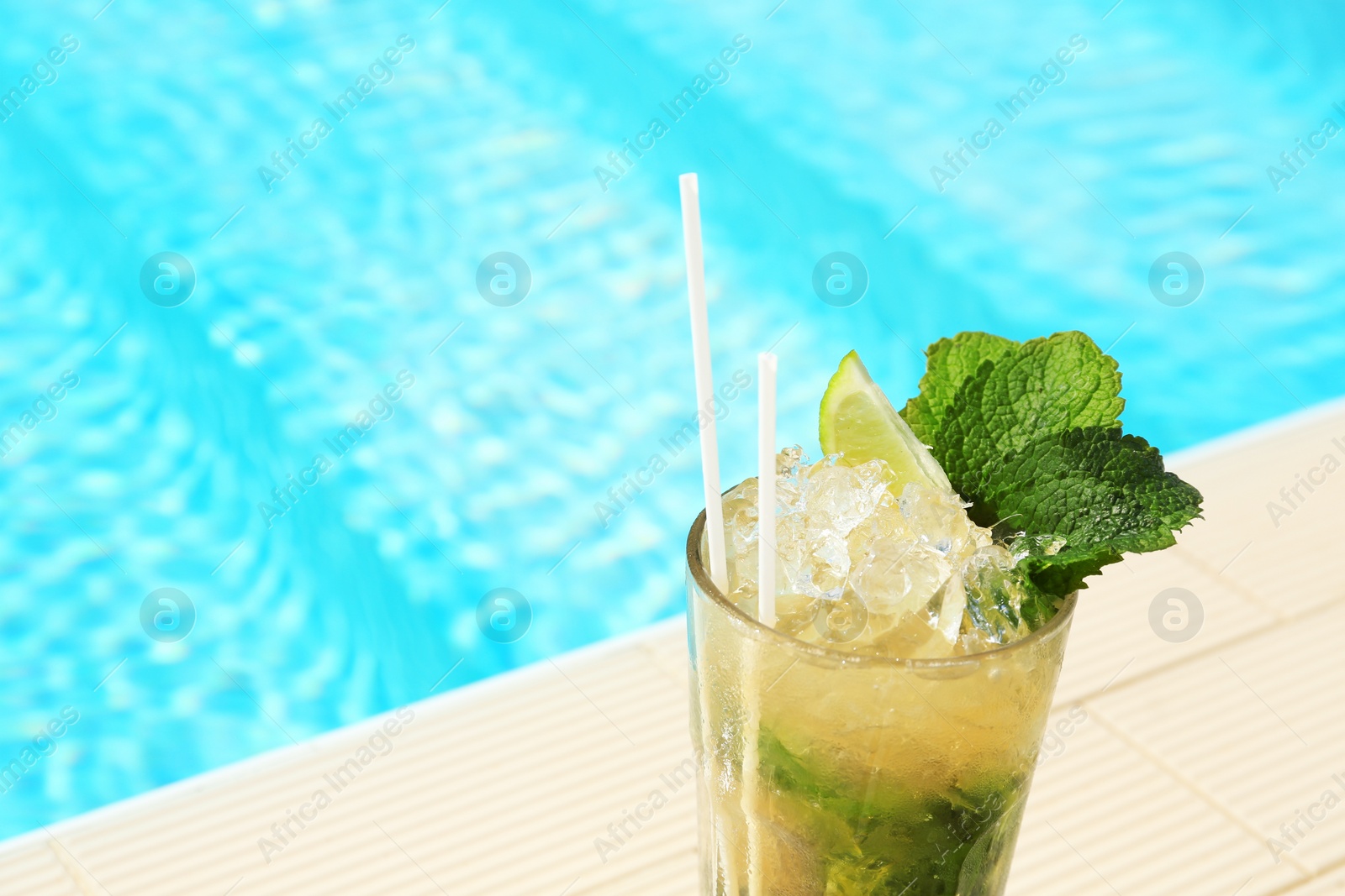 Photo of Glass of delicious mojito near swimming pool, space for text. Refreshing drink