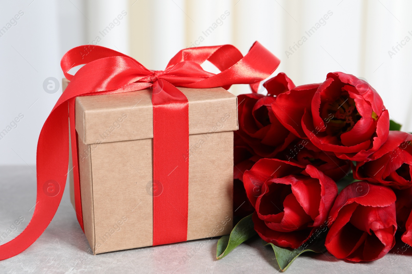 Photo of Beautiful gift box and bouquet of red tulip flowers on light table, closeup