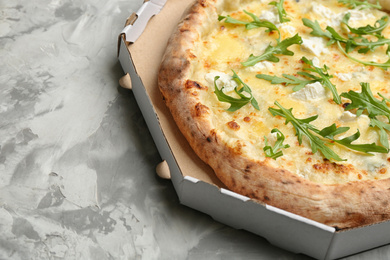 Photo of Delicious cheese pizza with arugula in takeout box on grey table, closeup
