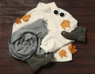Flat lay composition with sweater and dry leaves on brown wooden background. Autumn season